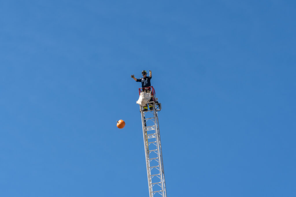 7 - A Salt Lake City firefighter drops a pumpkin from a ladder truck (SLCPD photo | October 27, 2023).