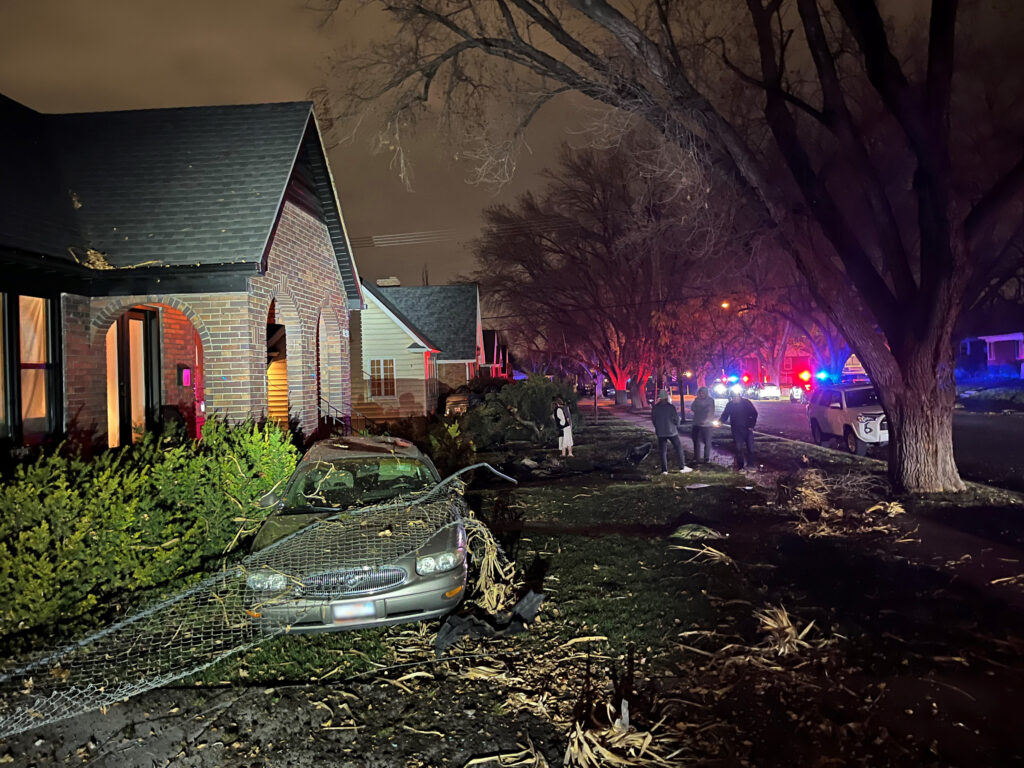 Photo: A tan car in the front yard of a house after a SUV crashed into it (SLCPD photo, November 30, 2023).