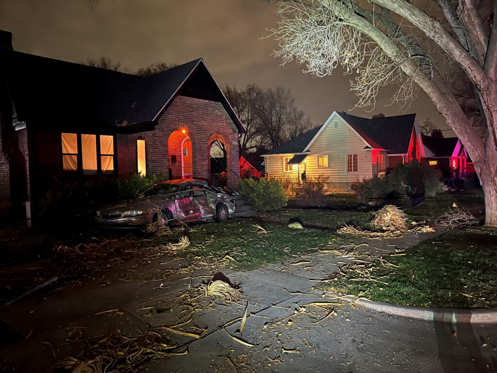 Photo: A tan car sits in the front yard of a house after a SUV crashed into it (SLCPD photo, November 30, 2023).