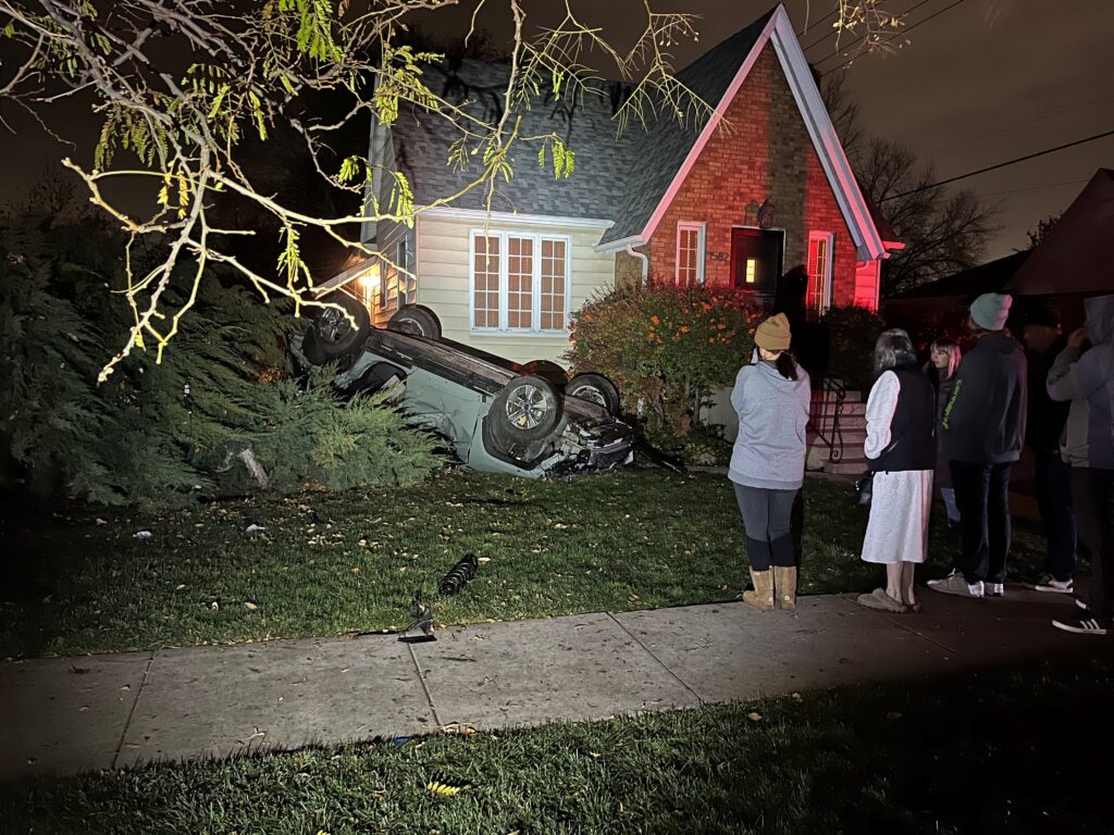 Photo: A green SUV on its roof in the front yard of a house after crashing into two parked cars and rolling over (SLCPD photo, November 30, 2023).